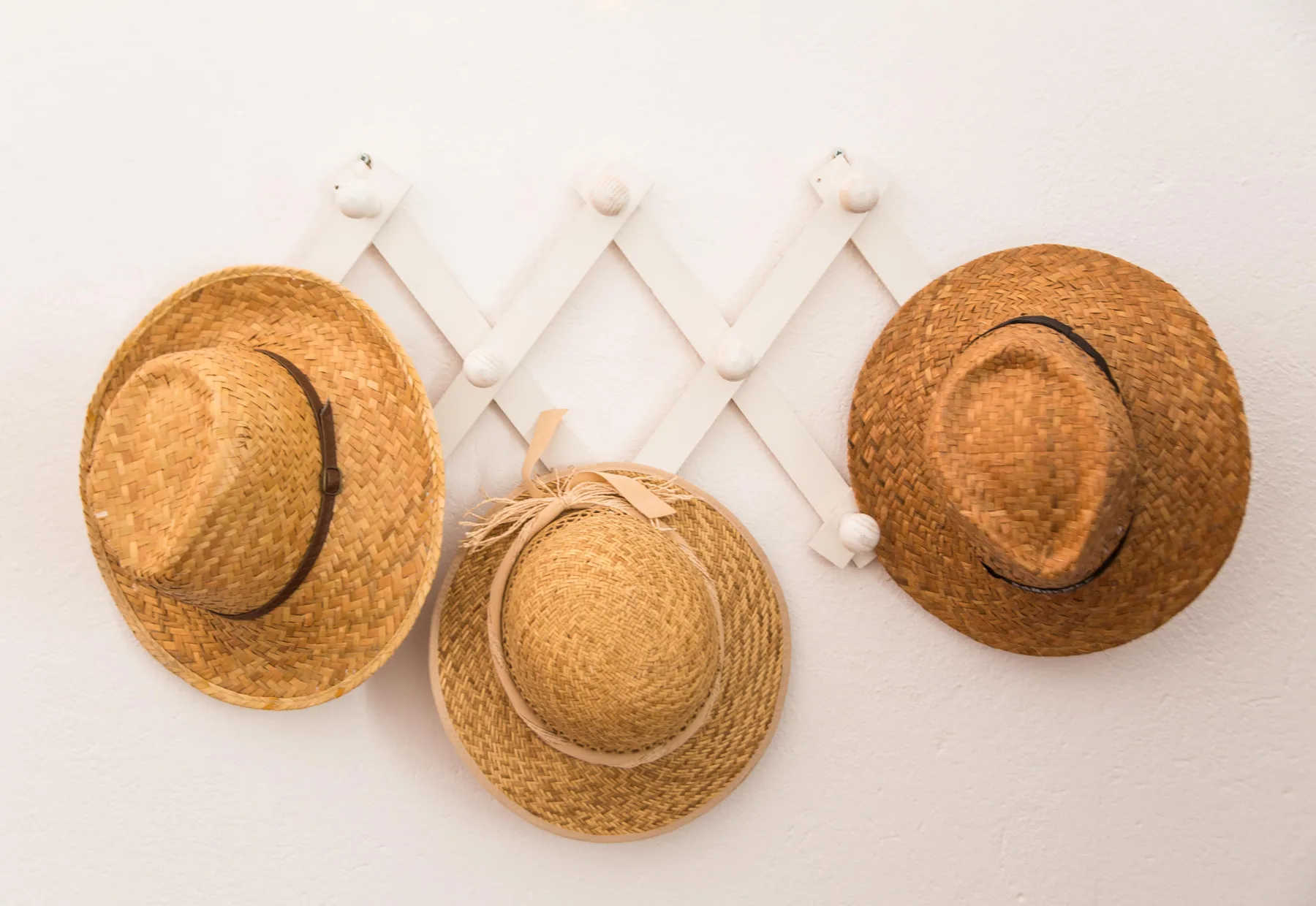 Tres sombreros de paja cuelgan de un perchero blanco en la pared.
