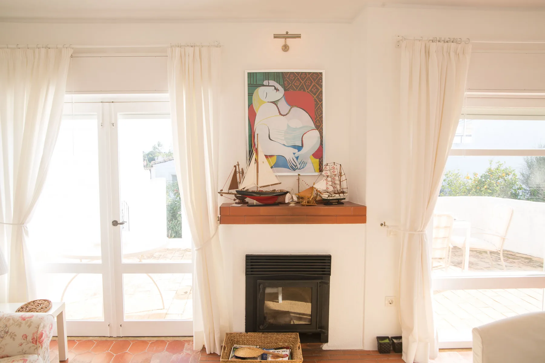 Una sala luminosa con chimenea y puertas acristaladas con cortinas que dan a una terraza.