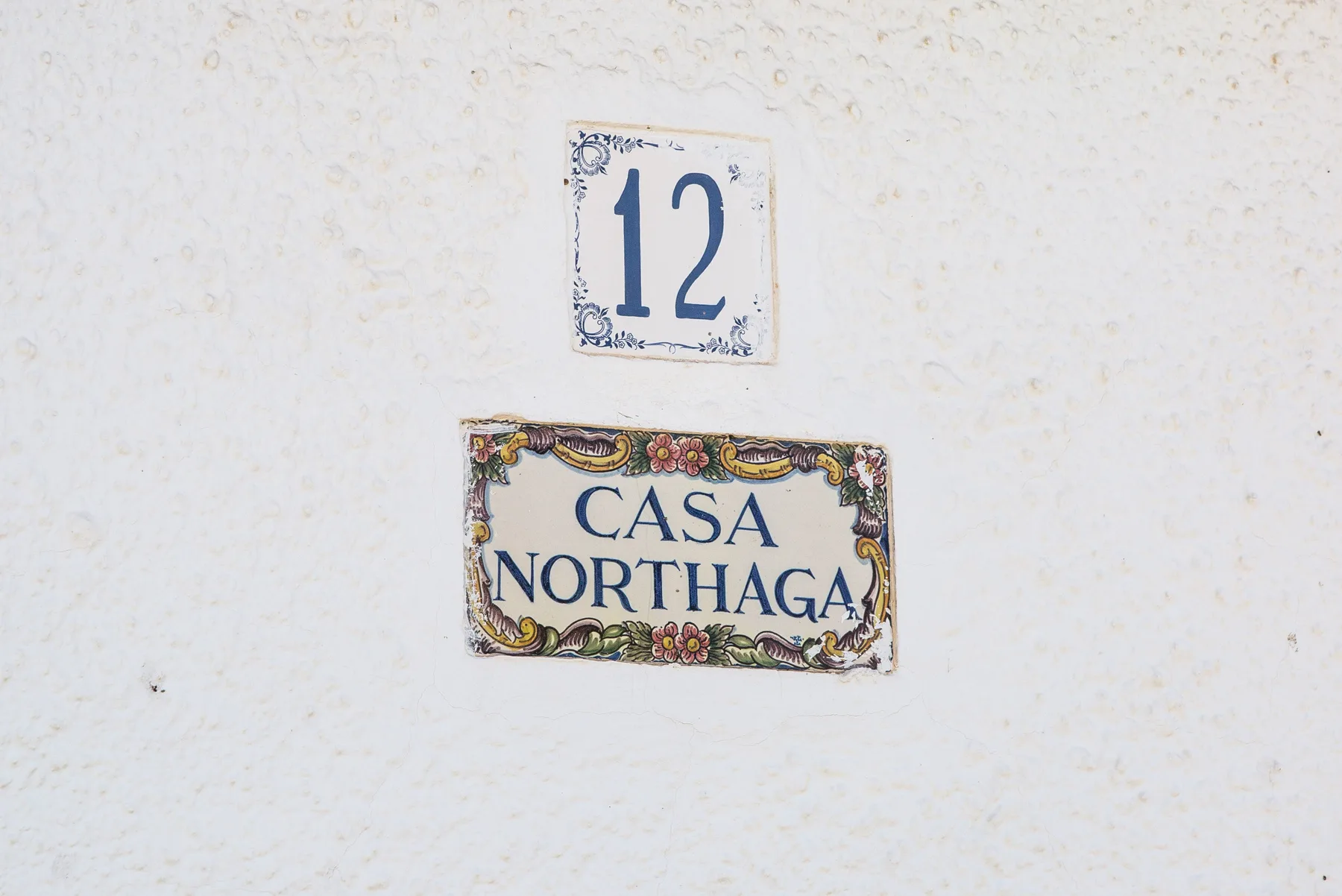 Una pared blanca muestra una placa con un número sobre un letrero decorativo de Casa Northaga.