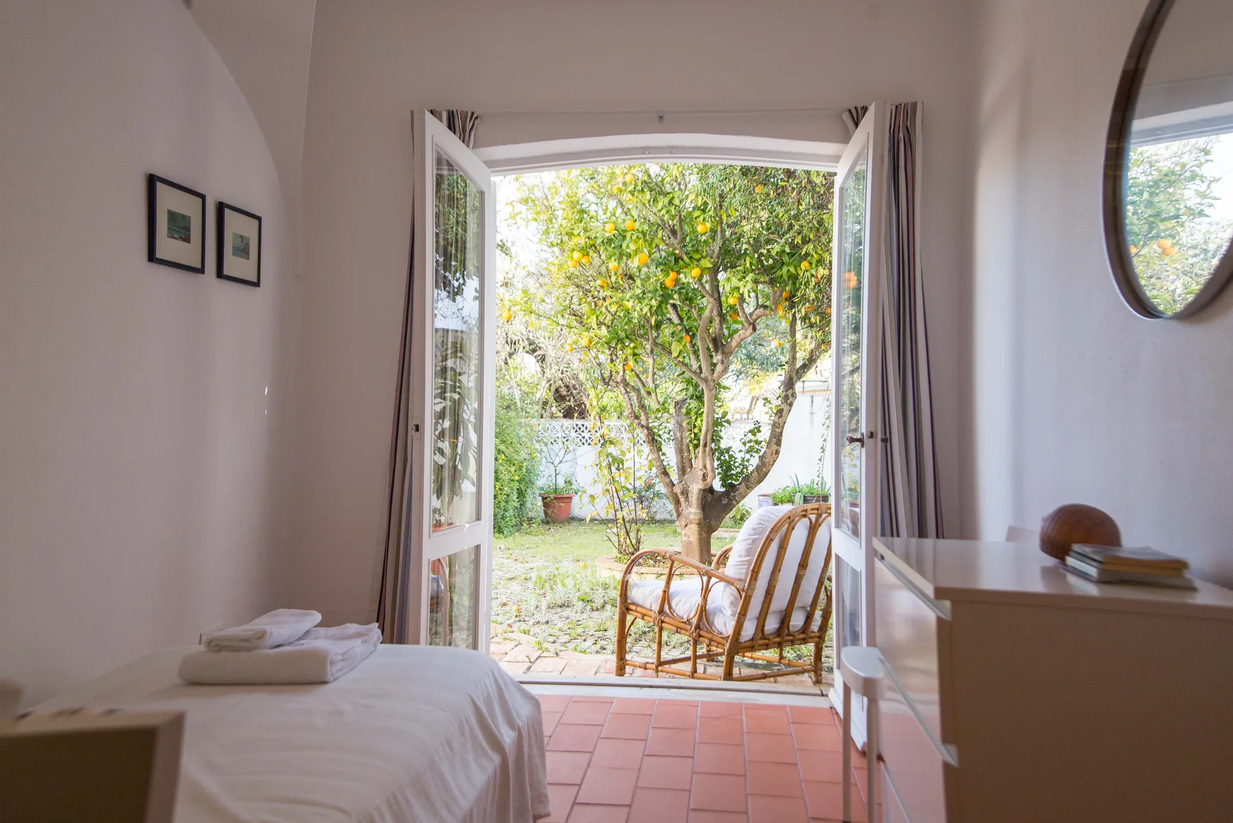 Un dormitorio se abre al jardín por unas puertas acristaladas, con asientos de mimbre.