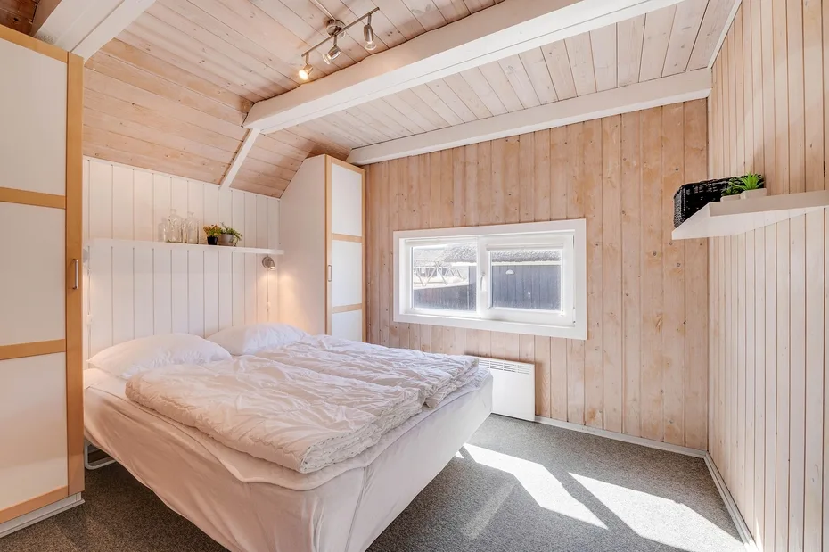 Un dormitorio luminoso con una cama bajo una ventana pequeña.