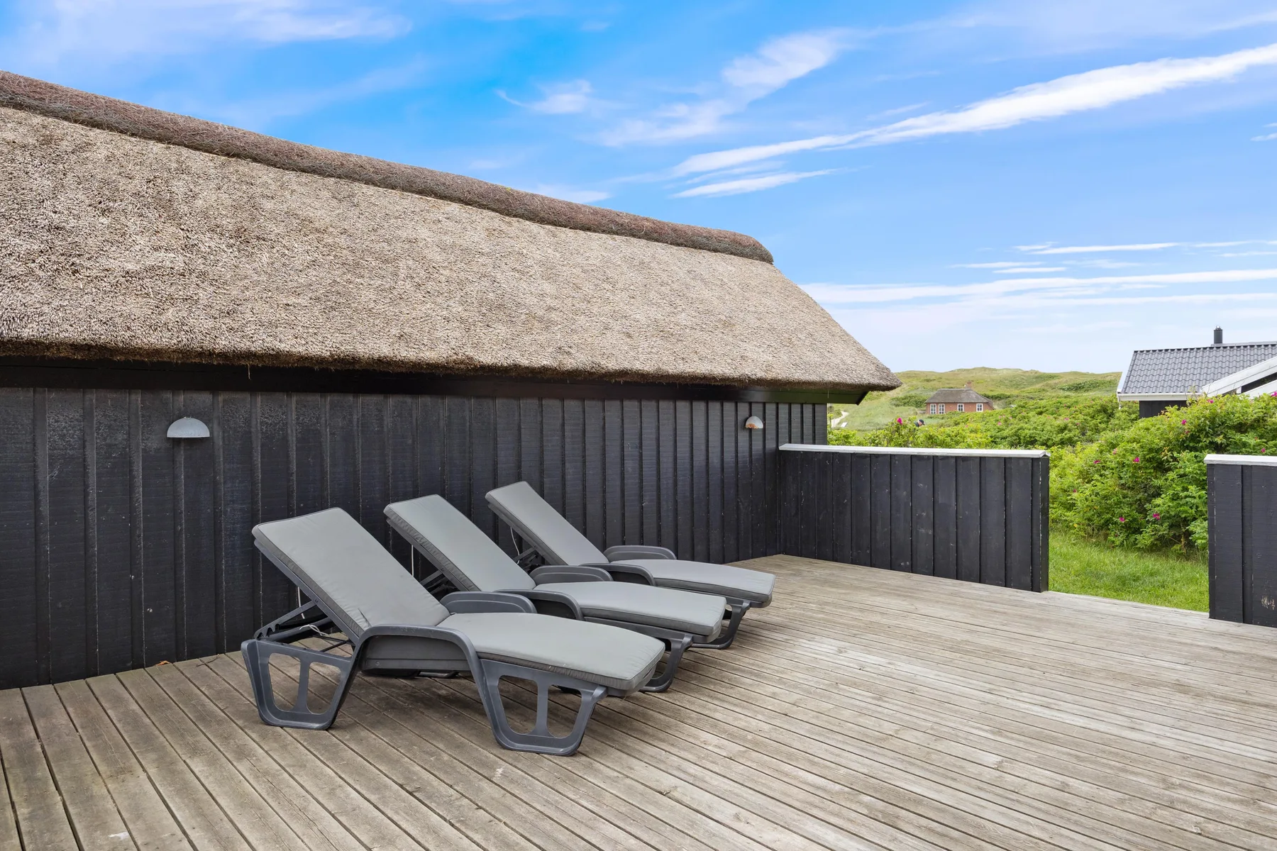 Una terraza de madera junto a una casa oscura tiene varias tumbonas reclinables.