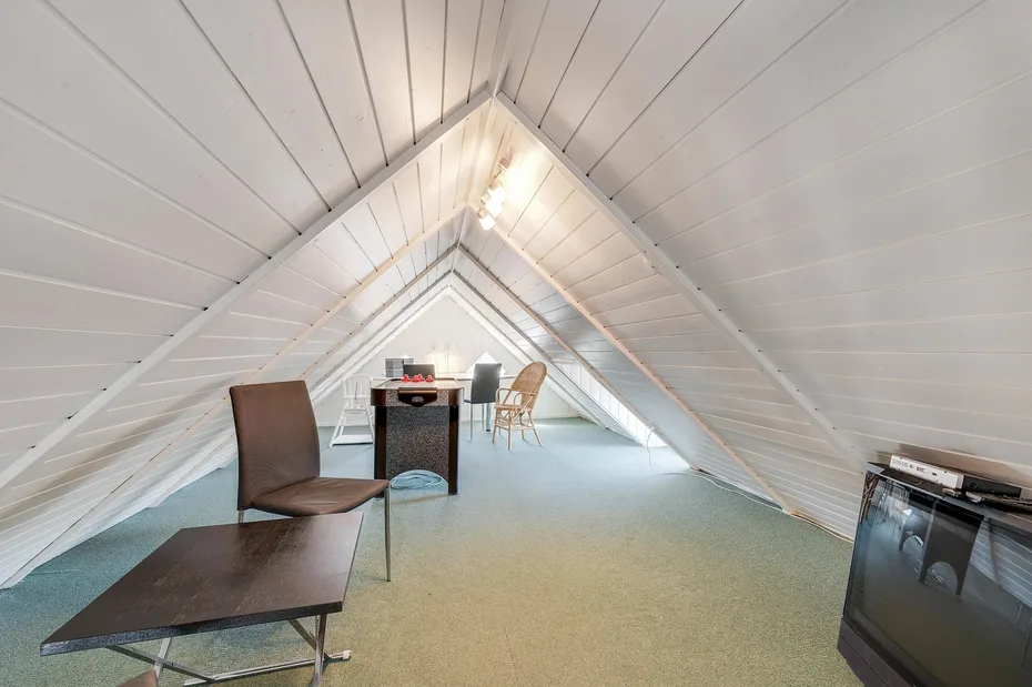 Una habitación abuhardillada con escritorio, asientos y paredes blancas inclinadas.