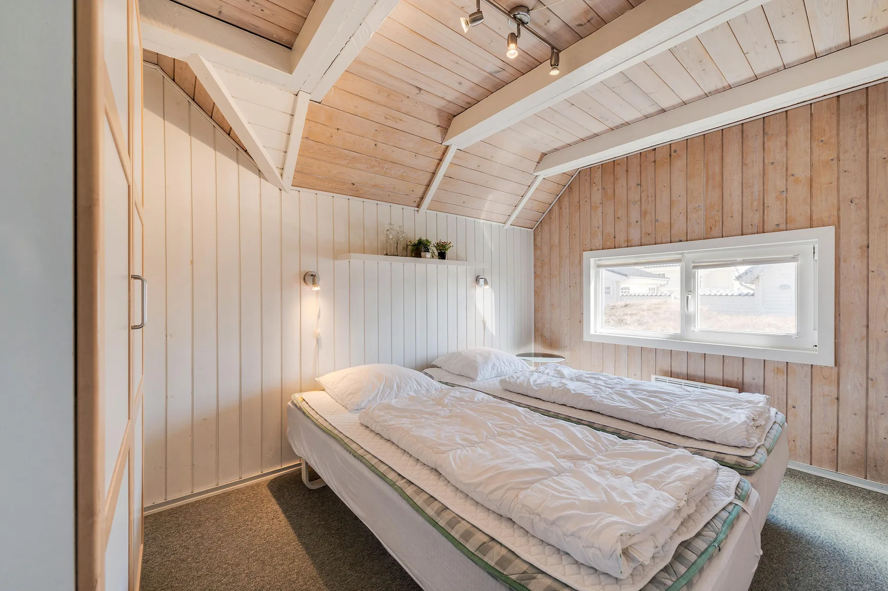 Un dormitorio con dos camas bajo un techo inclinado de paneles de madera y una ventana.
