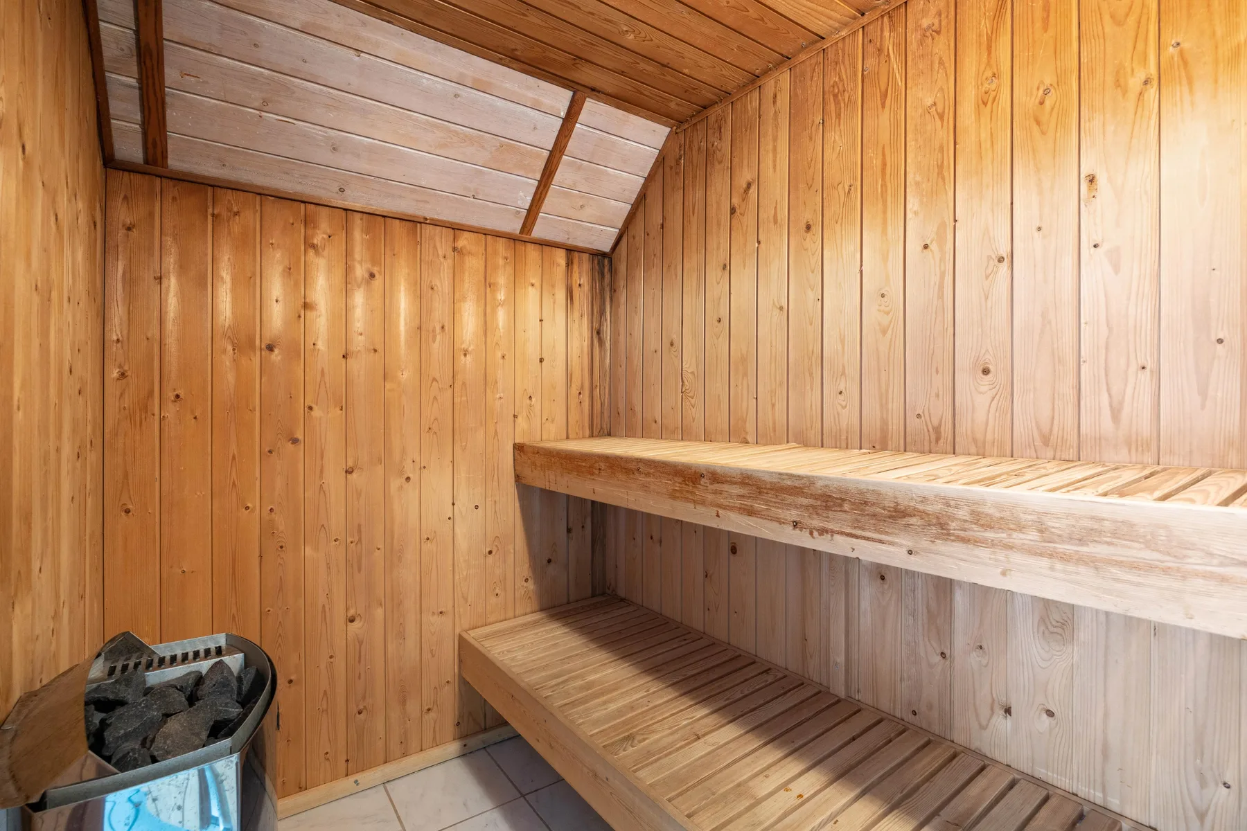 Una sauna revestida de madera con asientos escalonados y un calentador.