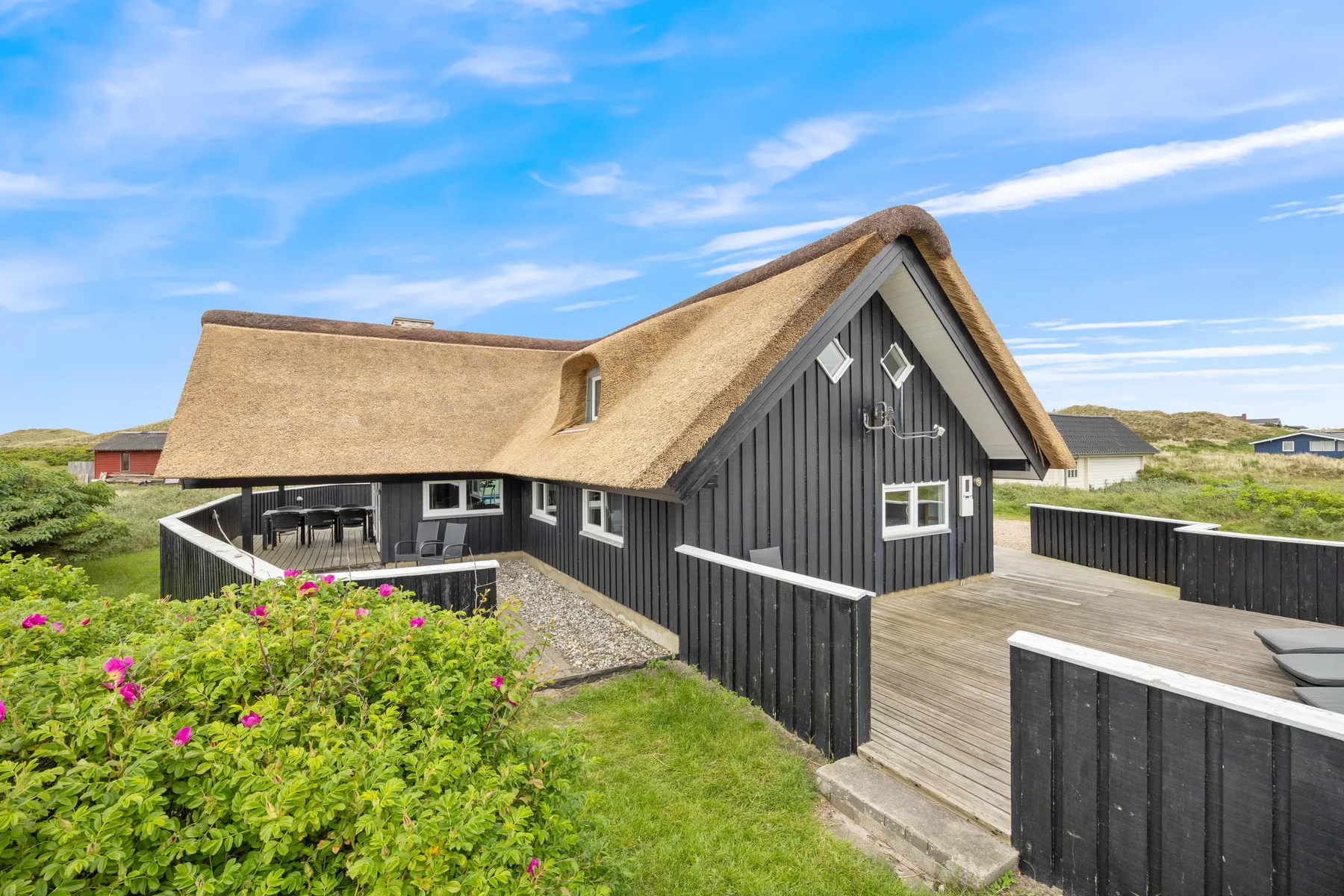 Una casa con techo de paja, exterior de madera oscura y terraza de madera.