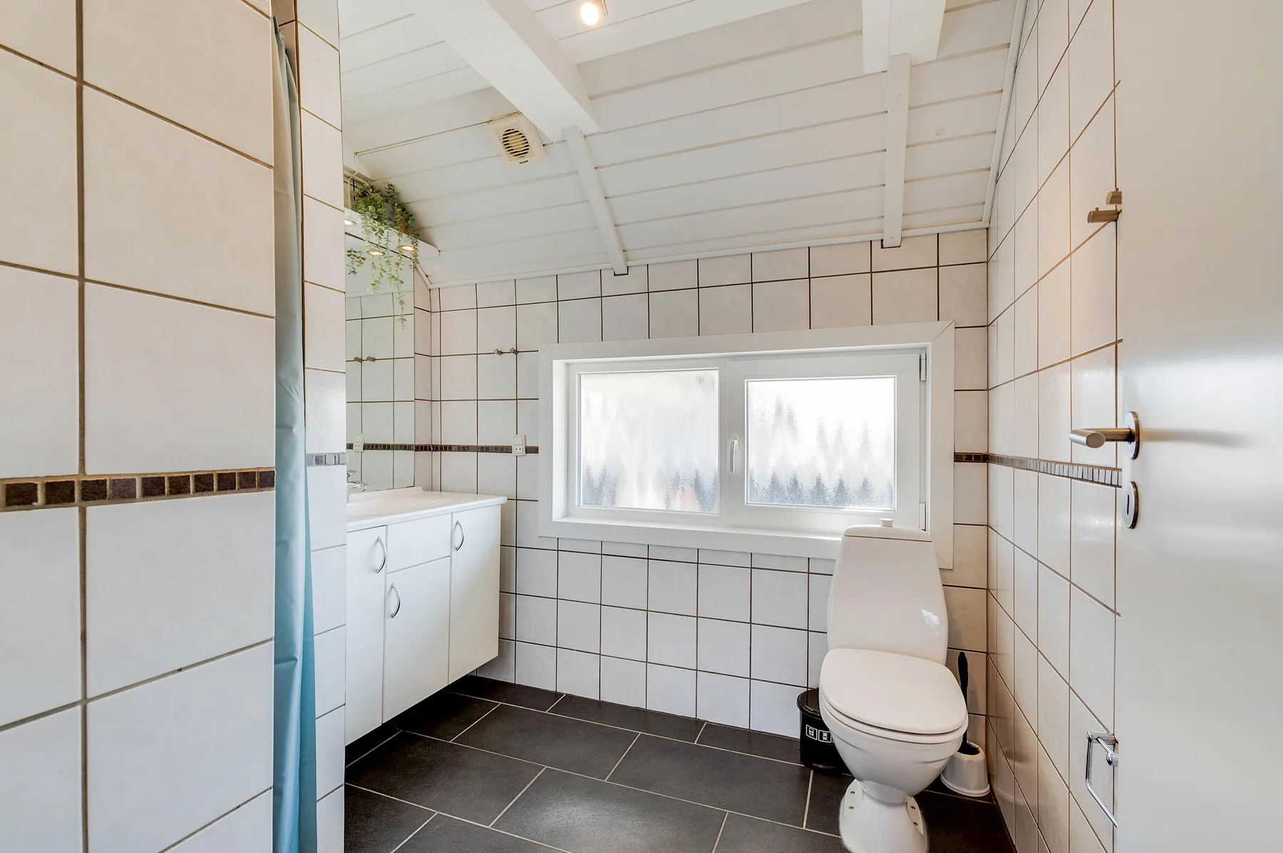 Un baño alicatado con inodoro, lavabo y una ventana esmerilada.
