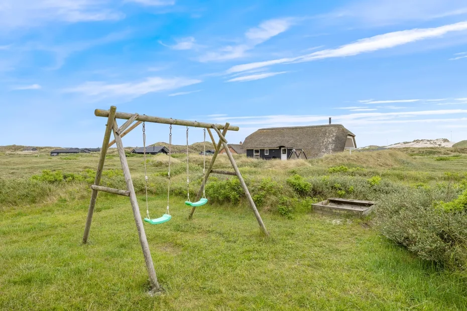 Un columpio de madera está en un campo cubierto de hierba, cerca de un edificio bajo.