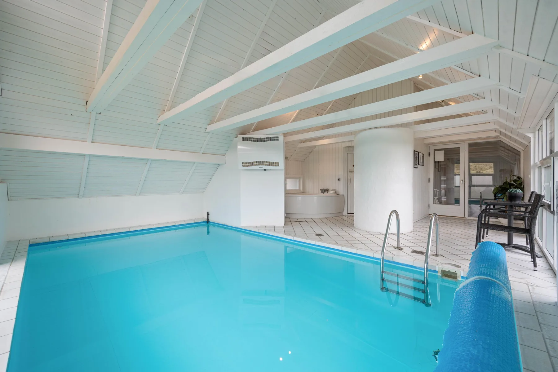 Una piscina cubierta con una zona de baldosas y asientos cerca.