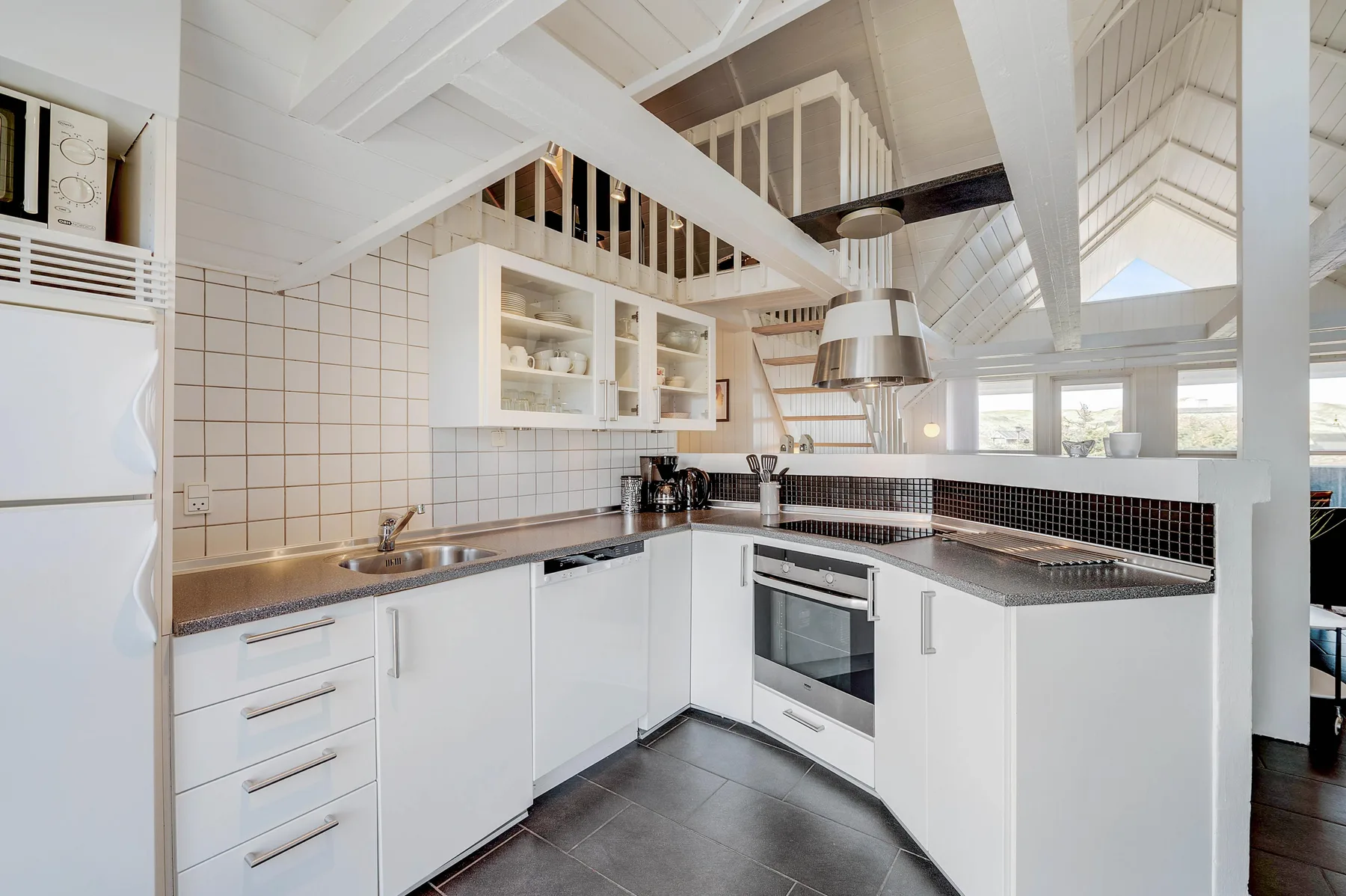 Una cocina luminosa con gabinetes blancos, encimeras oscuras y una zona de cocción central.