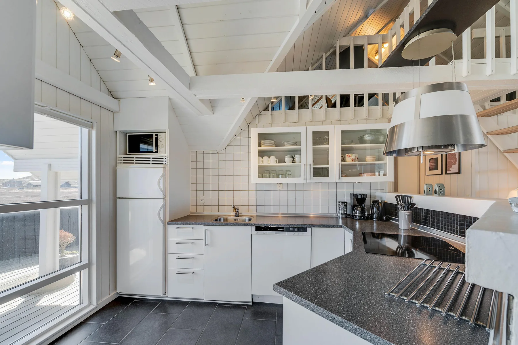 Una cocina luminosa con armarios blancos, una encimera oscura y grandes ventanas.