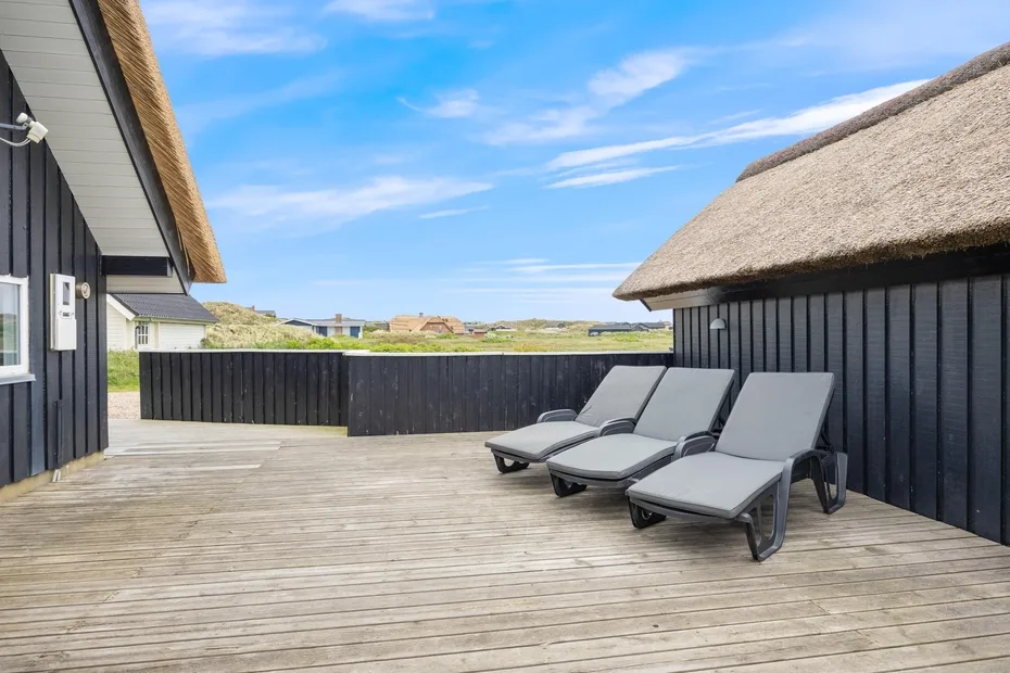Una terraza exterior de madera con sillas reclinables junto a un edificio de revestimiento negro.