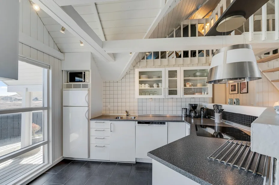 Una cocina luminosa con gabinetes blancos, paredes de azulejos y una encimera oscura.