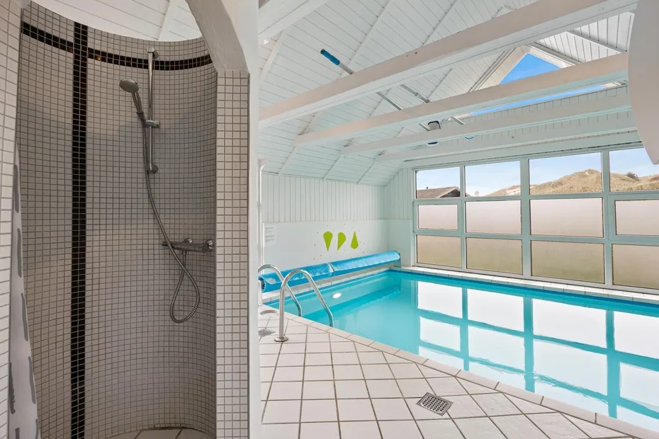 Una piscina cubierta con suelo de baldosas y una zona de ducha al lado.