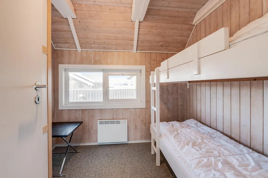 Un dormitorio compacto con literas, paredes revestidas de madera y una ventana.