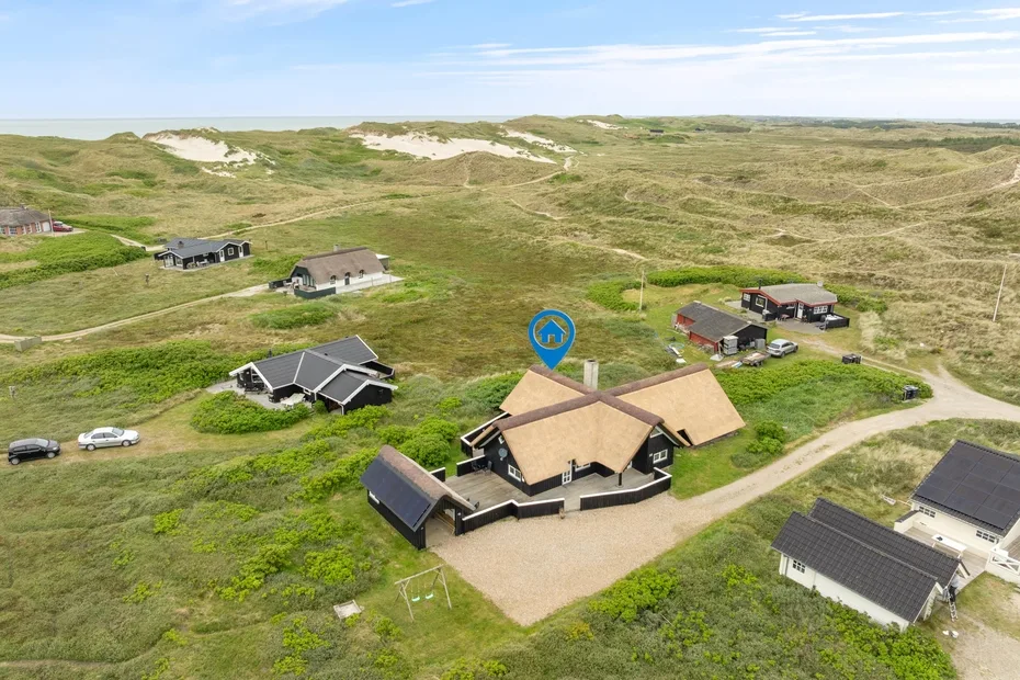 Vista aérea de varias casas dispersas entre dunas cubiertas de vegetación.