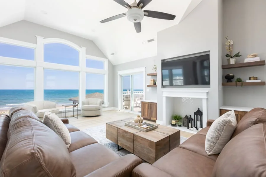 Una sala luminosa con una mesa de centro grande y vistas al mar por ventanas altas.