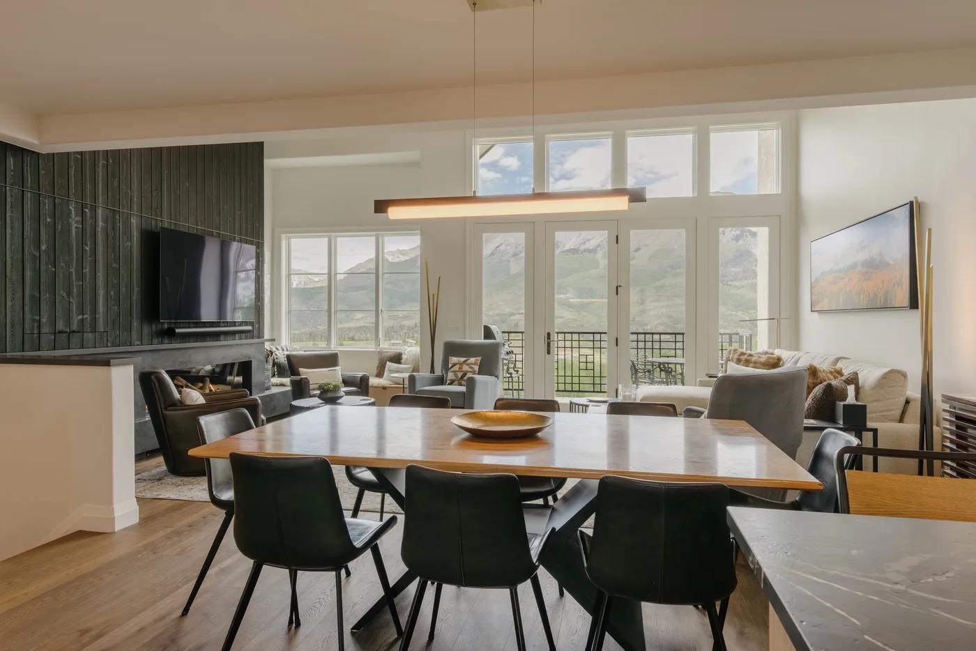 A bright dining and living area opens onto tall windows overlooking a mountain landscape.