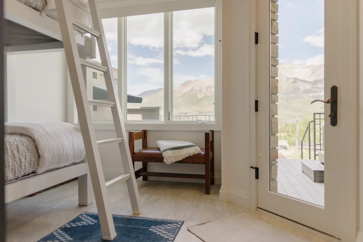 A bright bedroom with bunk beds, a small seating area, and mountain views through the windows.