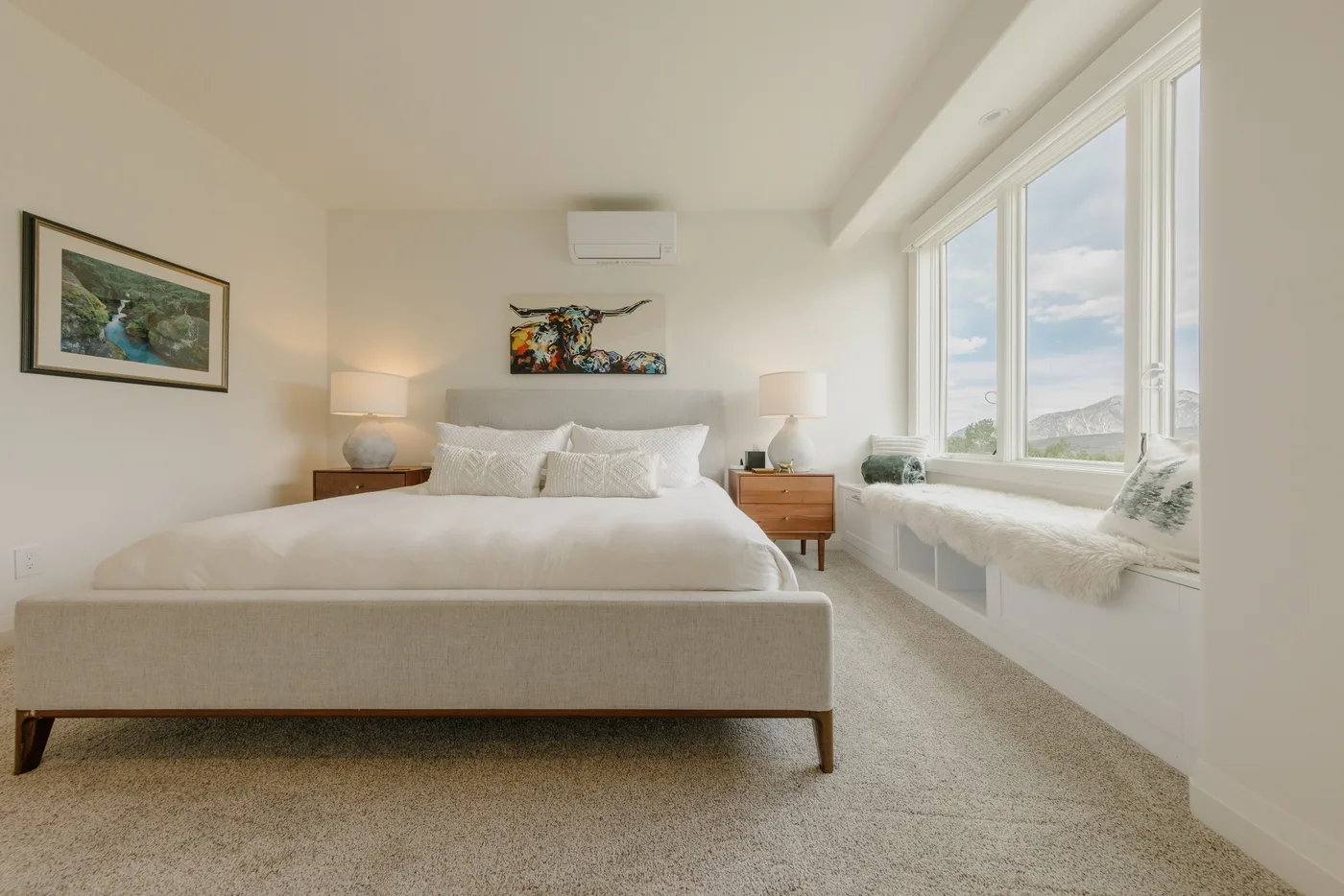 A bright bedroom with a neatly made bed and large windows.