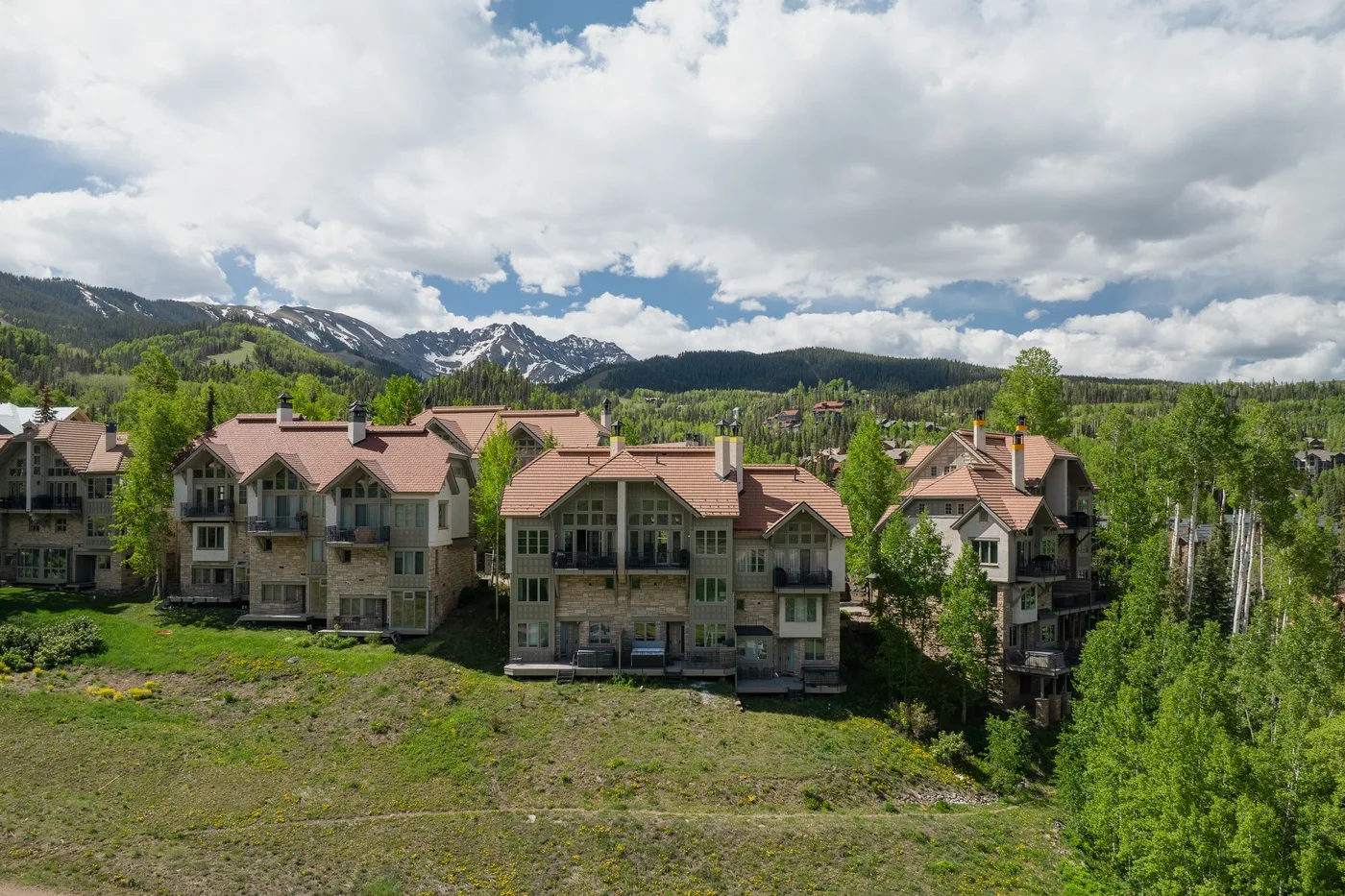 A cluster of mountain homes sits below forested slopes and snow-dusted peaks.