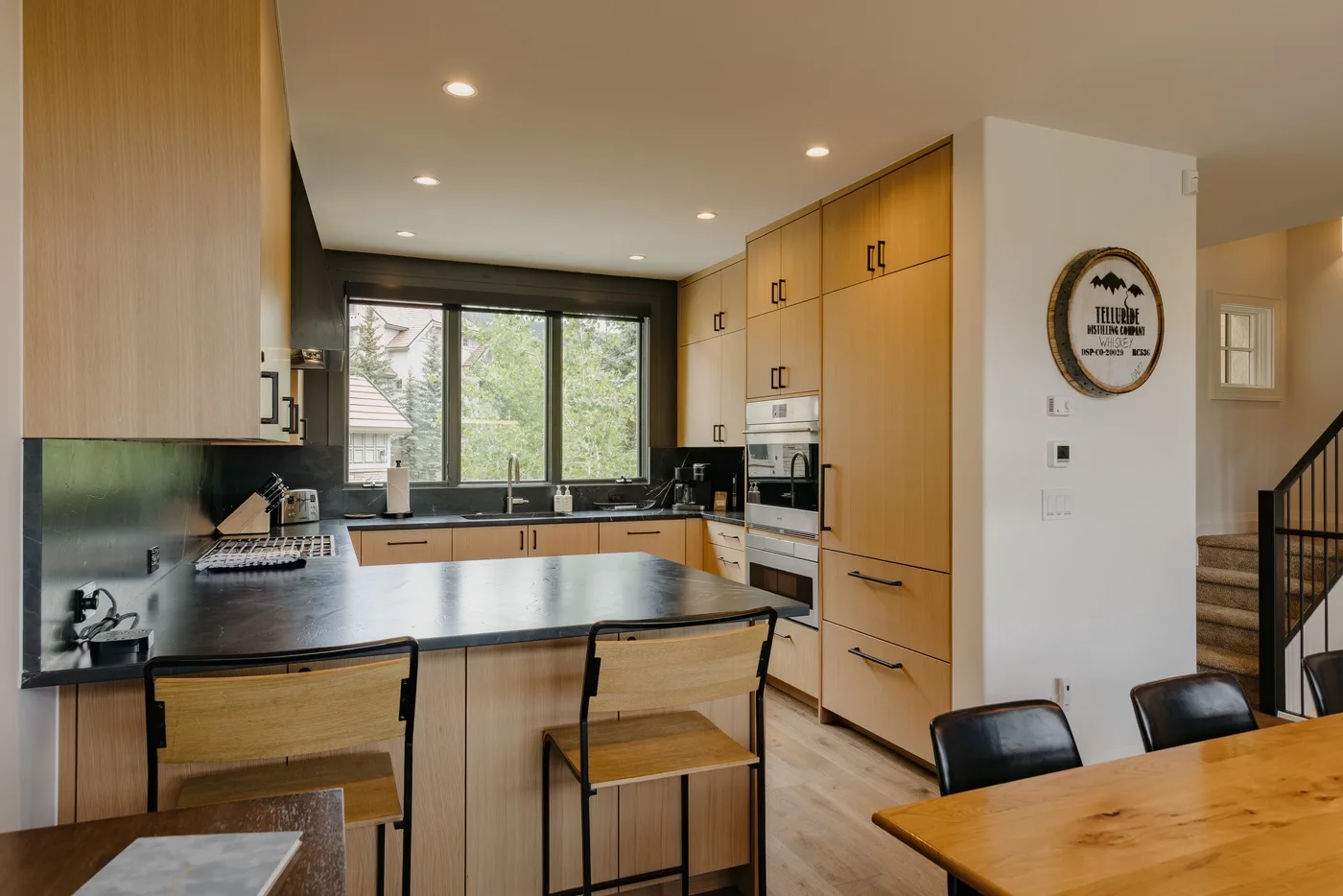A bright kitchen with wooden cabinetry, a central island, and windows overlooking greenery.
