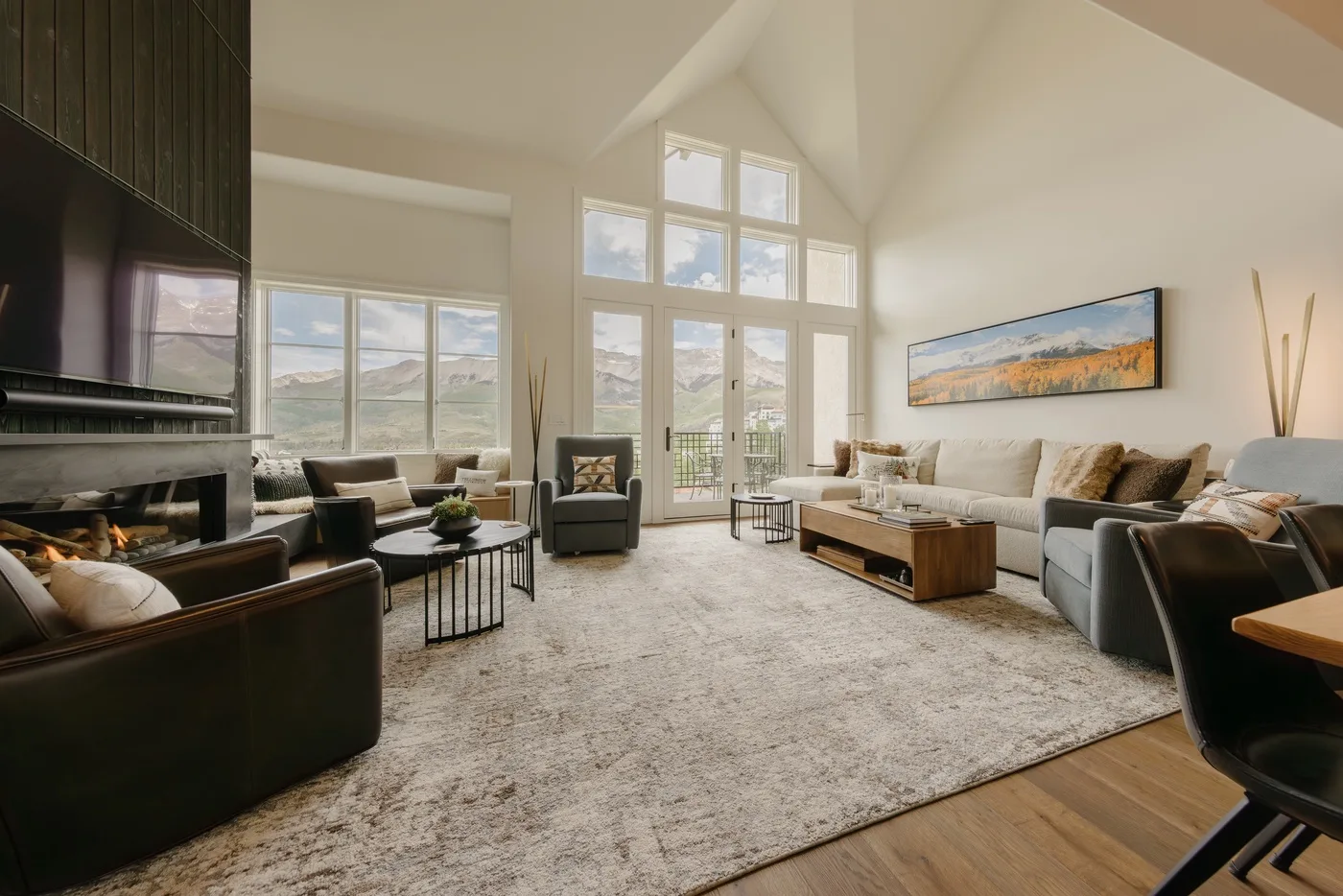 A spacious living room with seating arranged around a fireplace and tall windows.