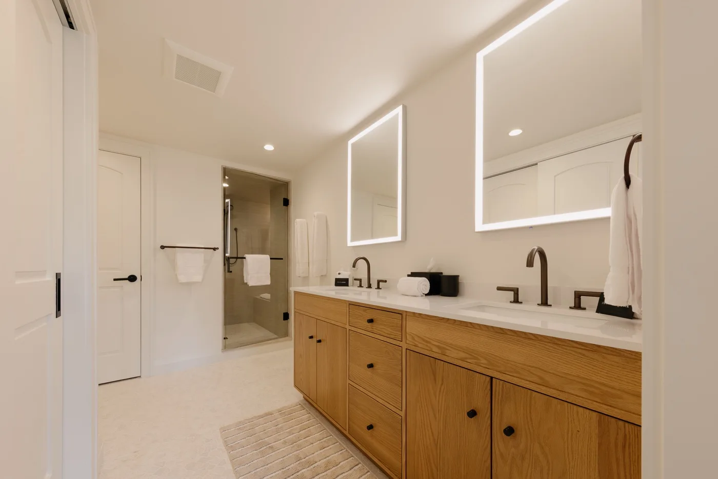 A bathroom with a long vanity, two sinks, and a glass shower.