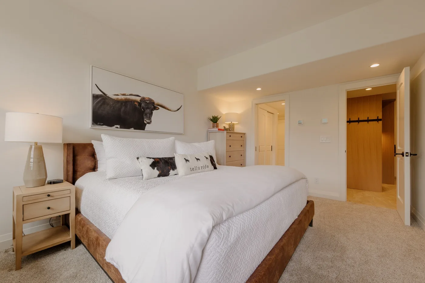 A bright bedroom with a neatly made bed and a framed bull artwork above it.