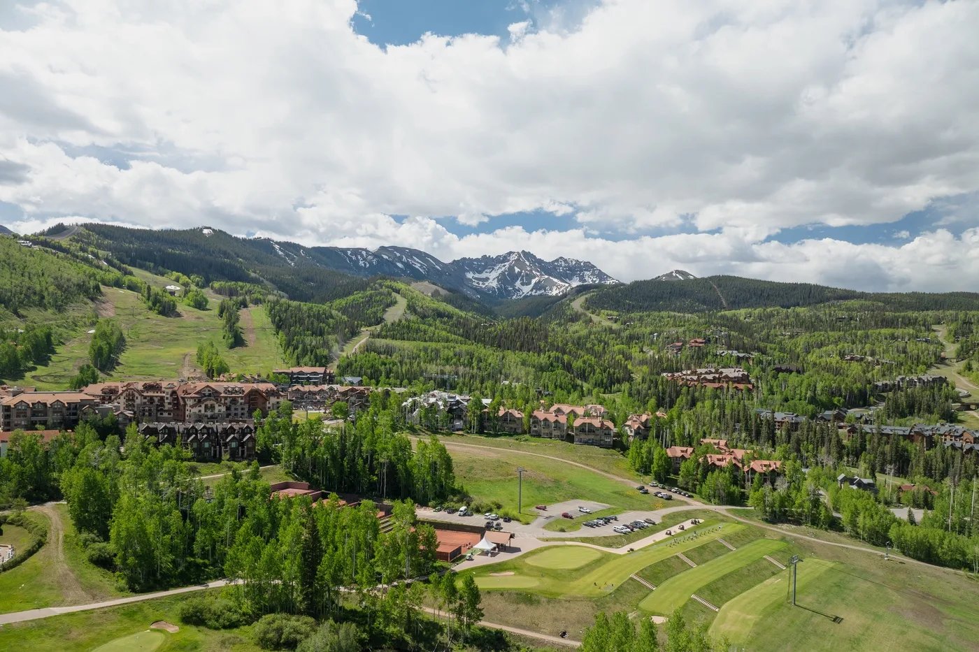 A mountain resort spreads across a green valley beneath snow-dusted peaks.