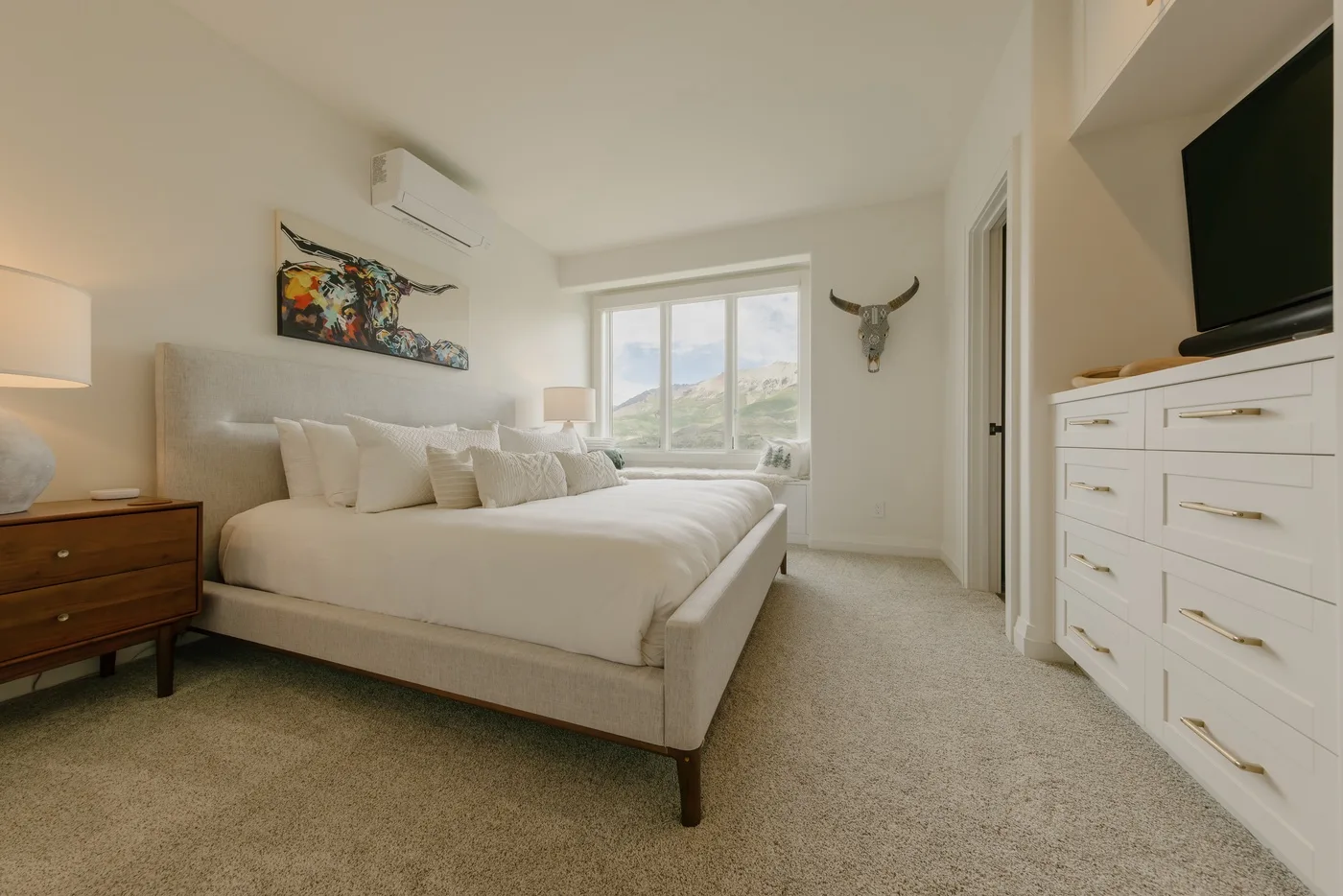 A bright bedroom with a bed, a window, and a television on a dresser.