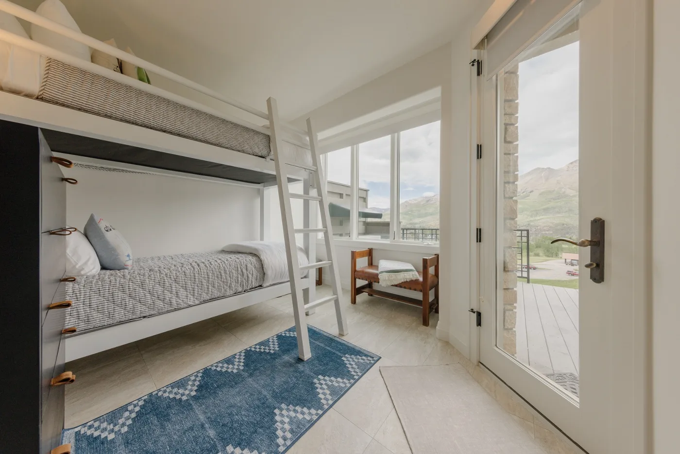 A bunk-bed room with a blue patterned rug and an open patio door.
