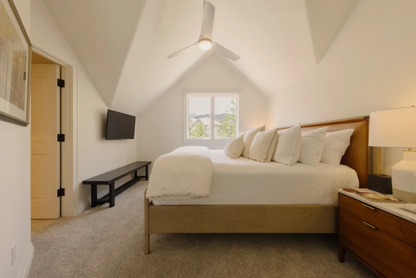 A bright bedroom with a large bed, a window, and a ceiling fan.