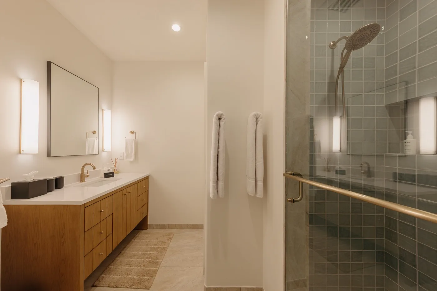 A bright bathroom with a long vanity and a tiled shower.