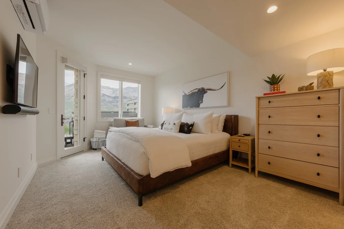 A bright bedroom with a neatly made bed and mountain views through the windows.