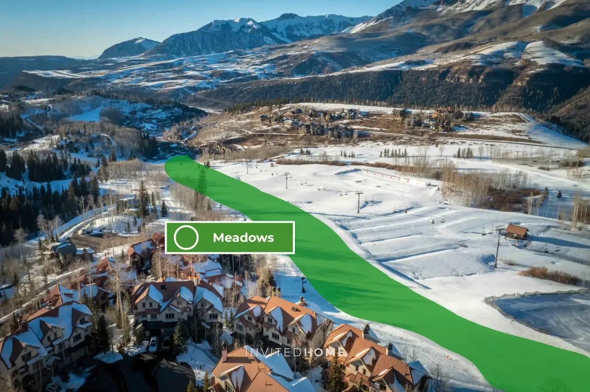 Snow-covered fields and buildings sit beneath a mountain range.