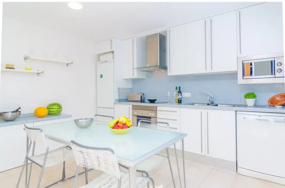 A bright white kitchen with a dining table and built-in appliances.