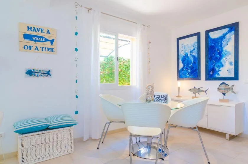 A bright dining area with a table, white seating, and blue coastal artwork.