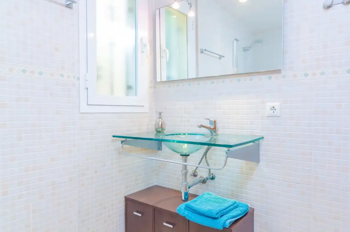 A tiled bathroom with a glass sink and wall mirror.