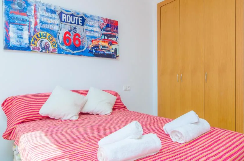 A bedroom with a red striped bed, folded towels, and a wooden wardrobe.