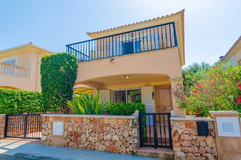 A two-story house with a balcony, stone wall, and gated entrance.