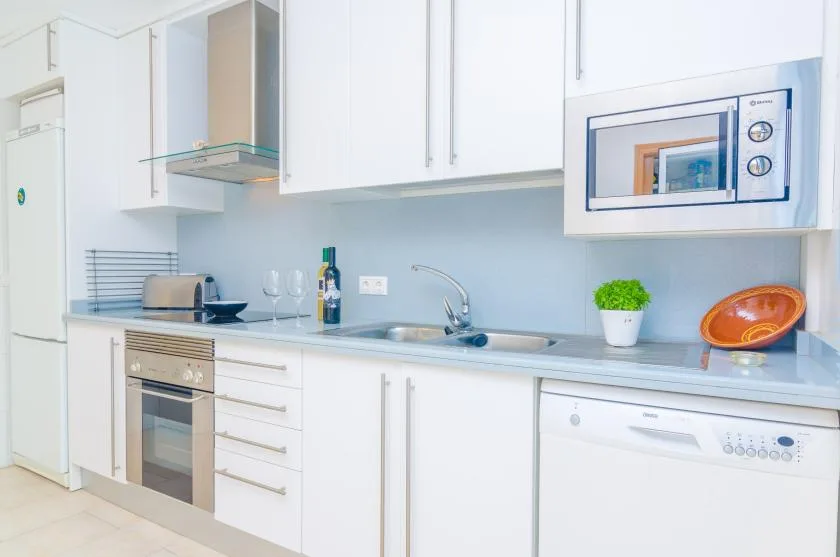 A bright white kitchen with a countertop, sink, and built-in appliances.