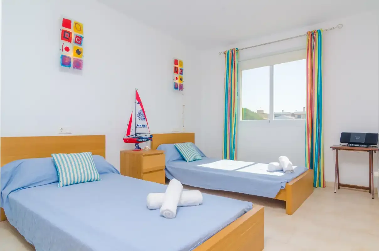 A bright bedroom with two beds and colorful curtains by the window.