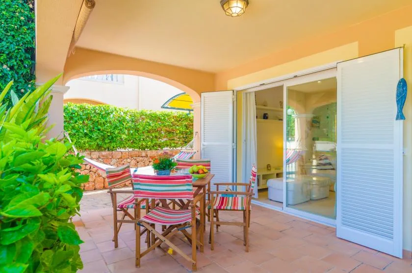 A covered patio with a striped outdoor dining set beside open doors.
