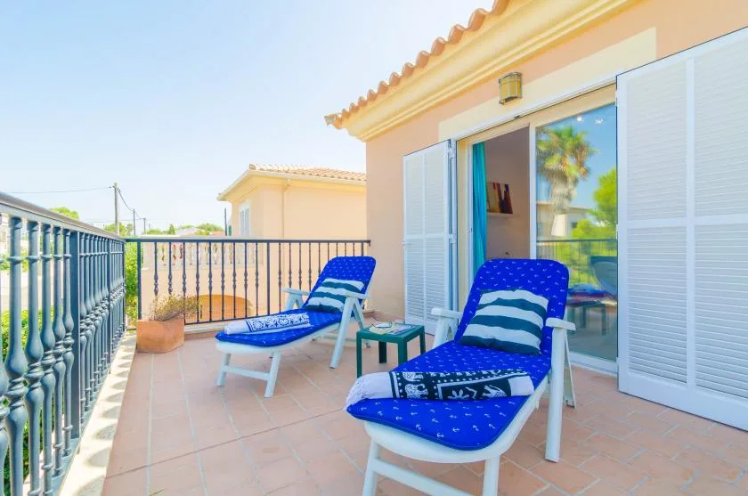 A sunny terrace has blue lounge seating beside an open glass door.