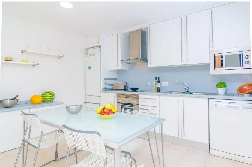 A bright kitchen with a central table and white cabinets.