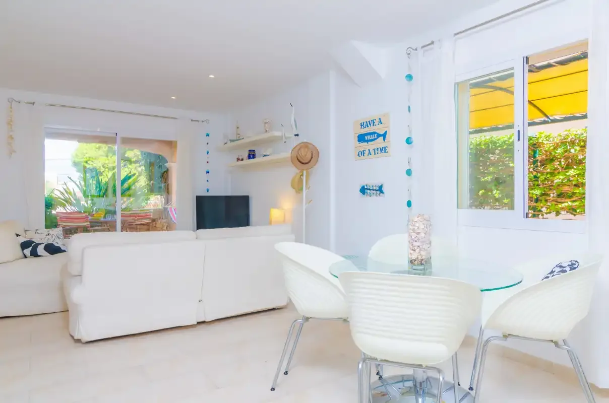 A bright living and dining area with white seating and a glass table.