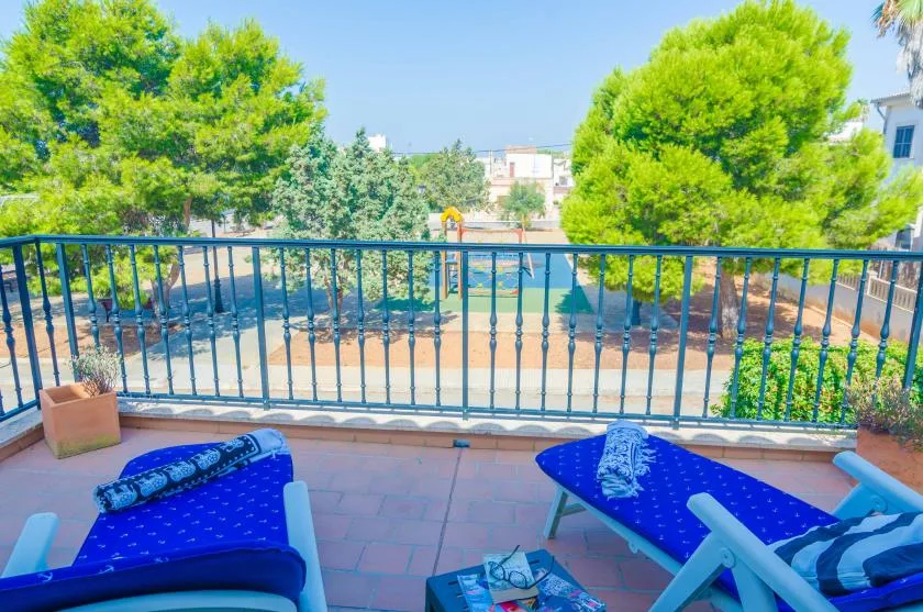 A balcony with blue lounge seating overlooks trees and a tennis court.