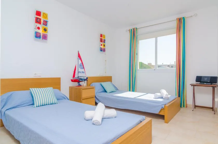 A bright bedroom with two beds, colorful curtains, and a model sailboat.