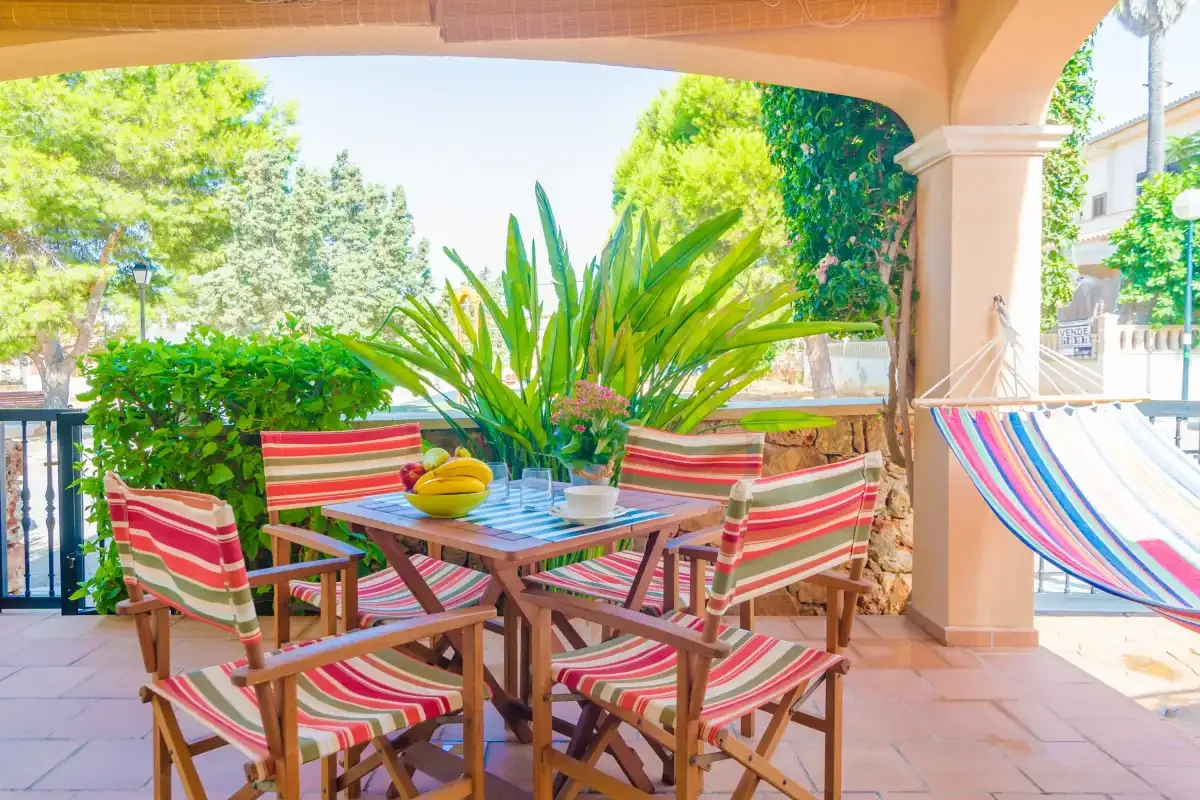 A covered patio has a striped outdoor dining set surrounded by greenery.